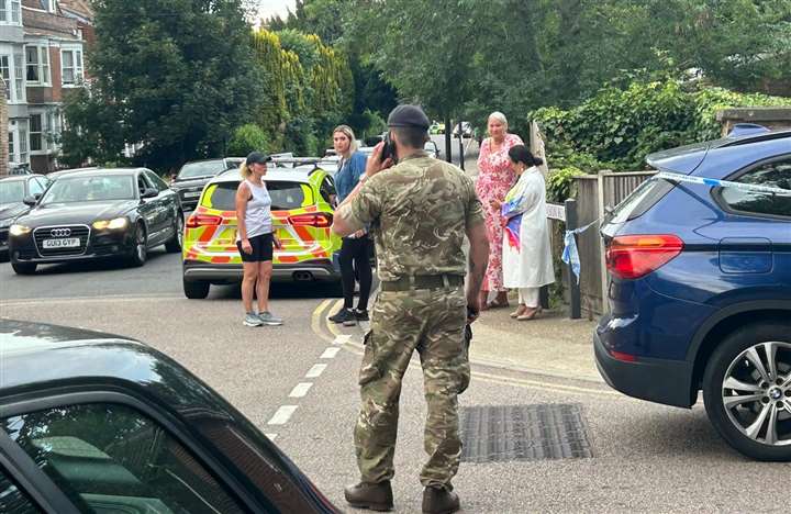 a soldier is taking a picture of a group of people standing on the side of the road .