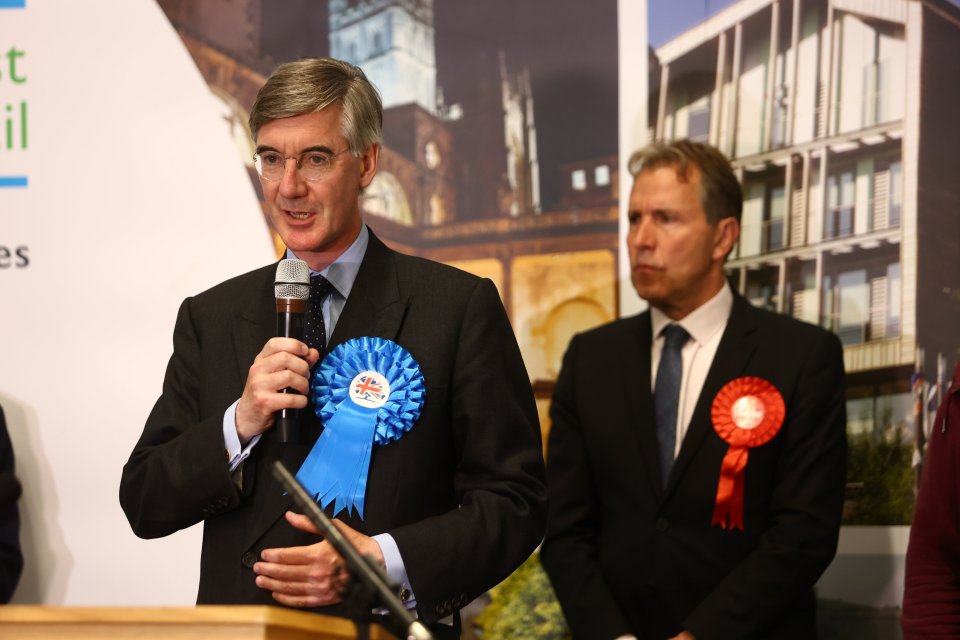 a man speaking into a microphone with a blue ribbon that says vote tory