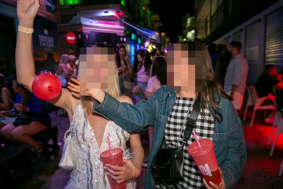 two women holding drinks in front of a sign that says irish town