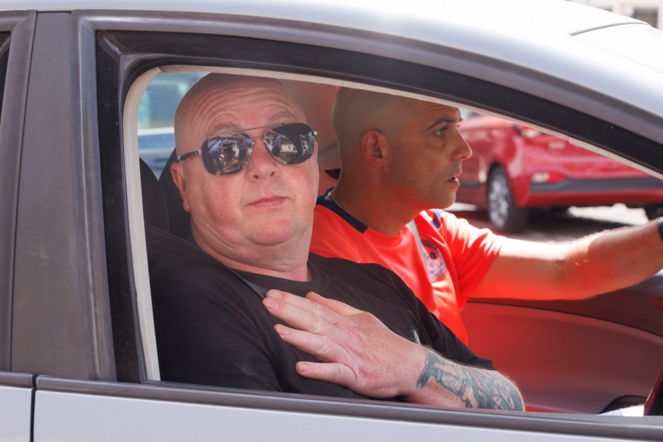 a man wearing sunglasses sits in a car next to another man