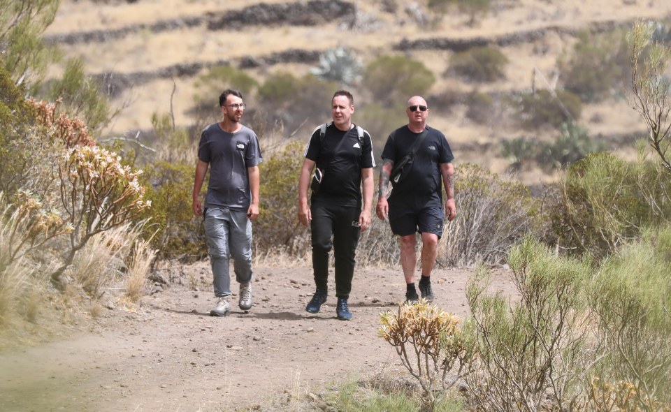 three men are walking down a dirt path and one of them is wearing an adidas shirt