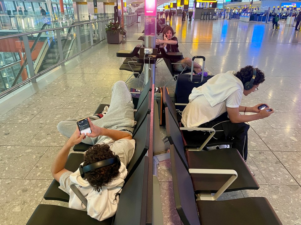 people are sitting in a waiting area at an airport looking at their phones