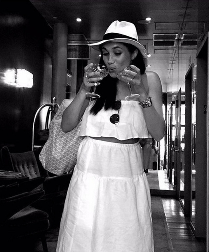 a woman in a white dress and hat is drinking from a glass