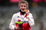 a woman wearing an adidas jacket holds a bouquet of flowers and a gold medal