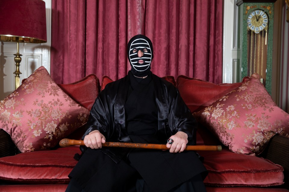a man wearing a mask sits on a couch holding a cane