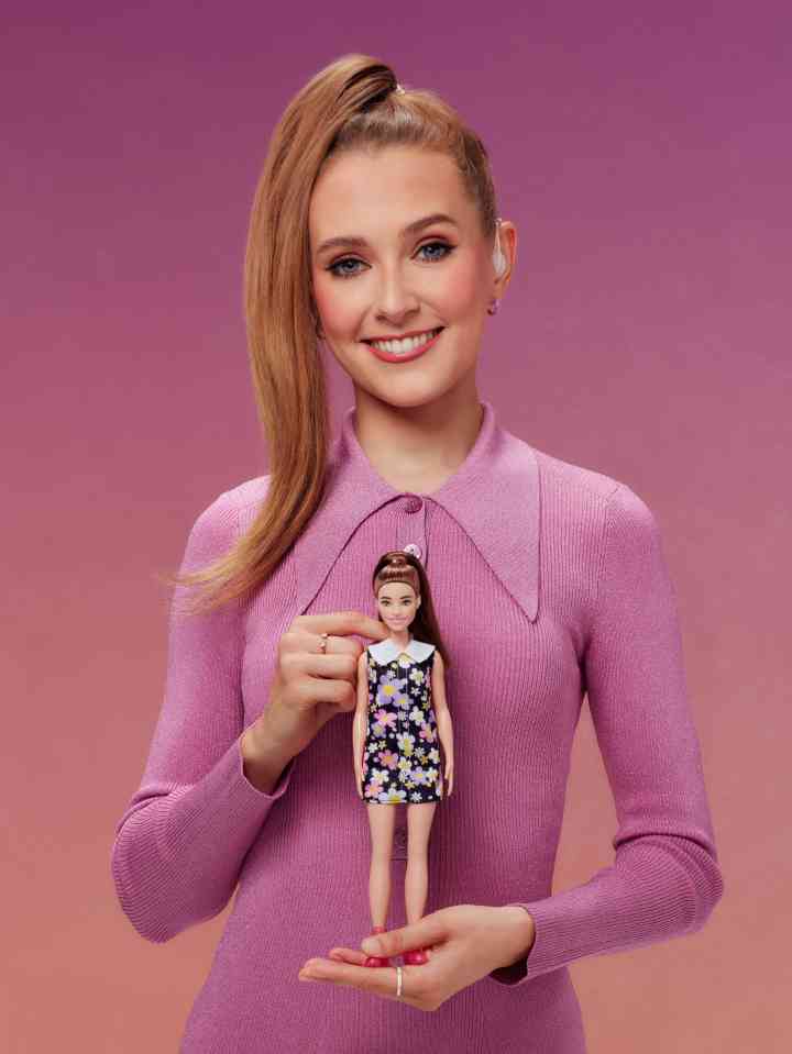 a woman in a purple sweater is holding a barbie doll