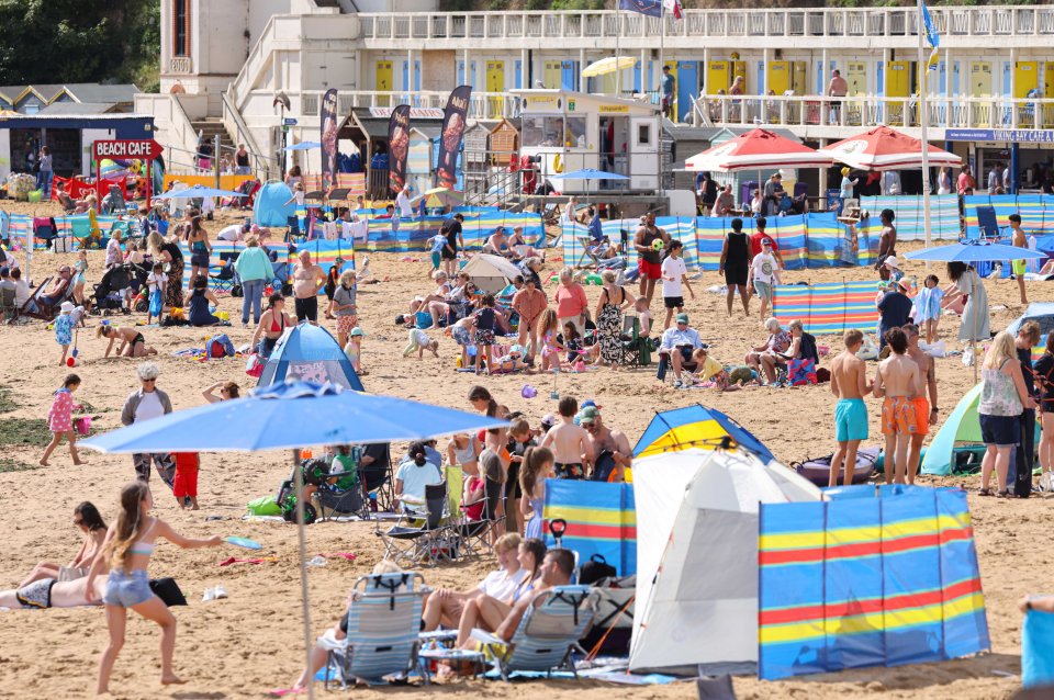 a beach filled with people and umbrellas including a beach cafe
