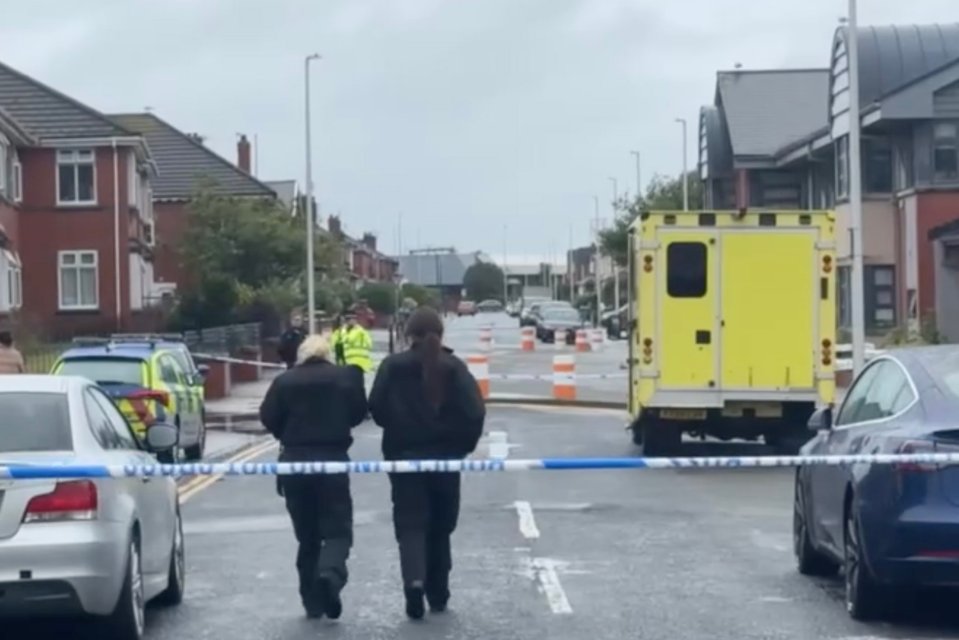 two police officers walk down a street behind a police tape