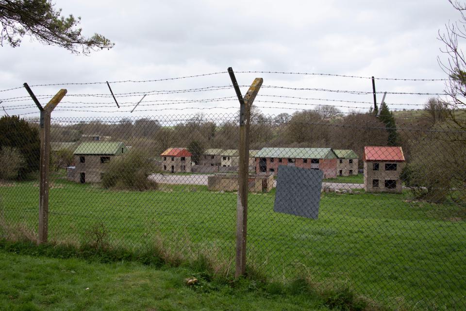 a barbed wire fence surrounds a field with houses in the background