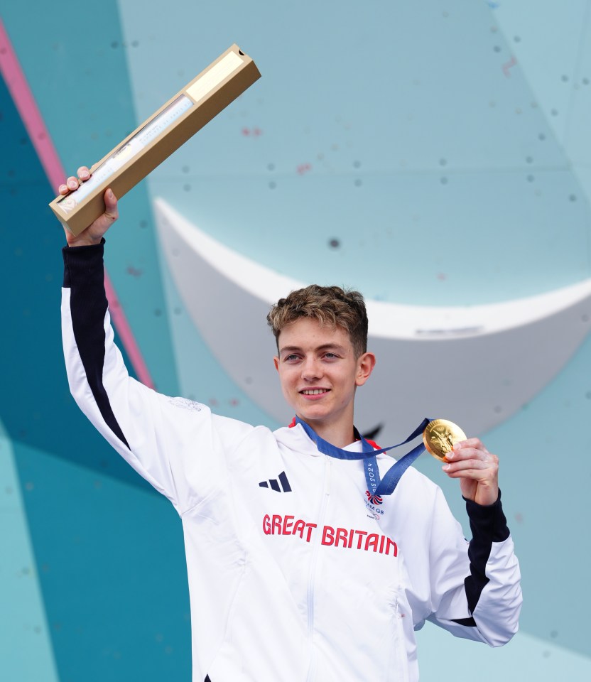 a young man wearing a great britain jacket holds up a gold medal