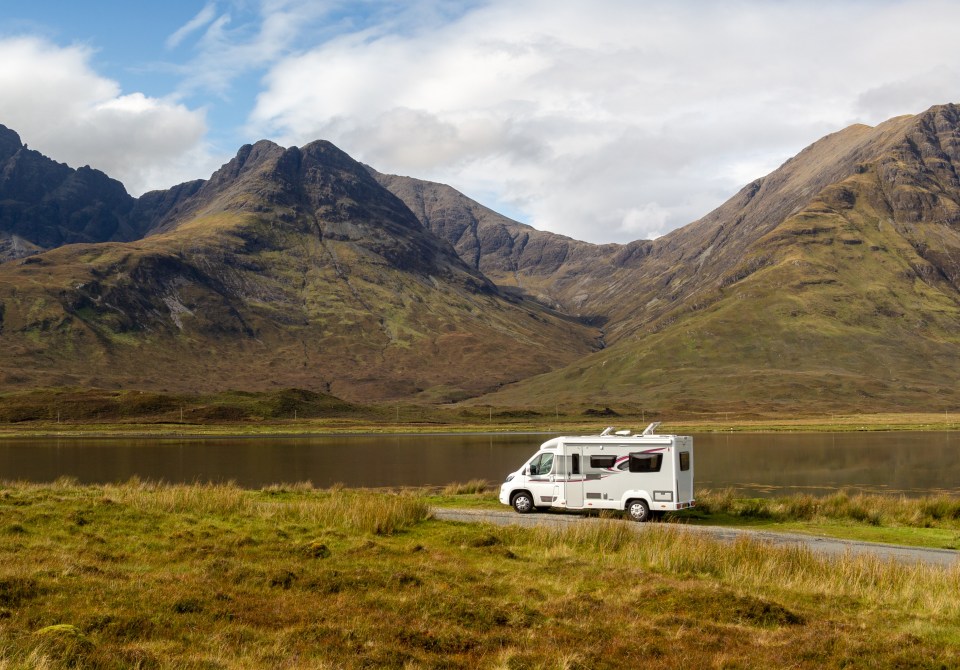 a man and woman sit in the back of a van near the beach