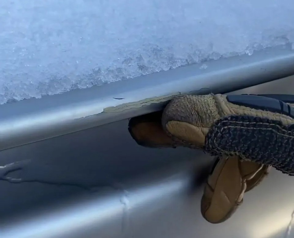 a person wearing gloves is reaching into the trunk of a silver car