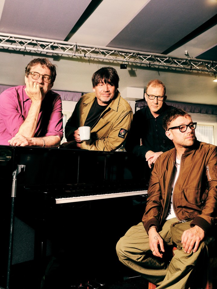 a group of men sitting around a piano with one man holding a cup