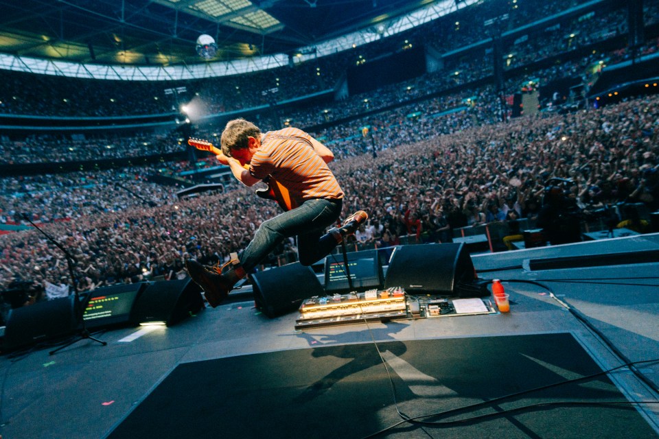 a man jumps in the air while playing a guitar in front of a crowd
