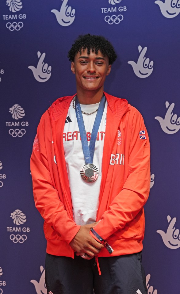 a man with a medal around his neck stands in front of a wall that says team gb