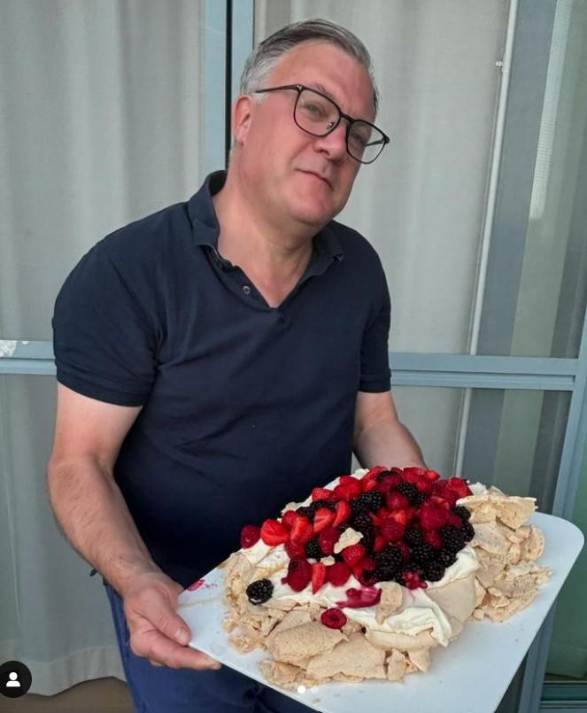a man with glasses holds a large cake with berries on top