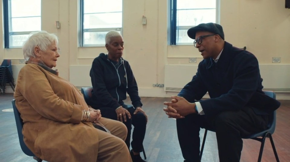 a man sits in a chair talking to two women
