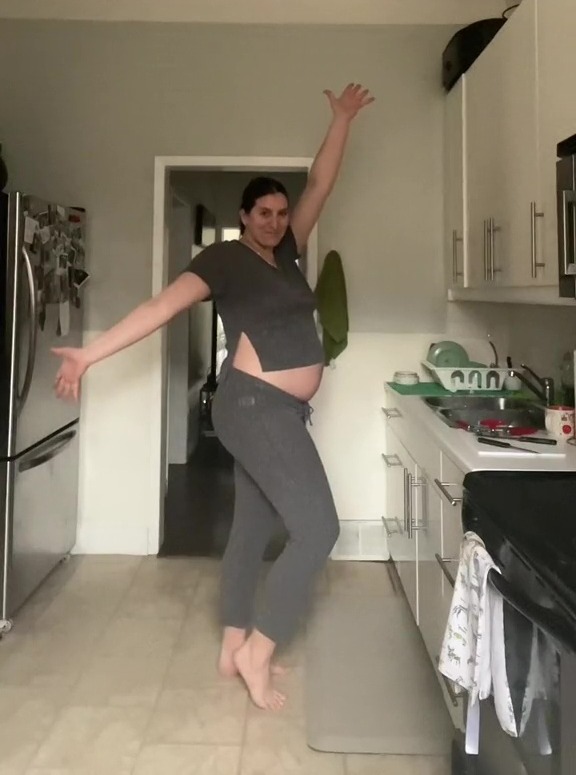 a pregnant woman is dancing in a kitchen with her arms outstretched