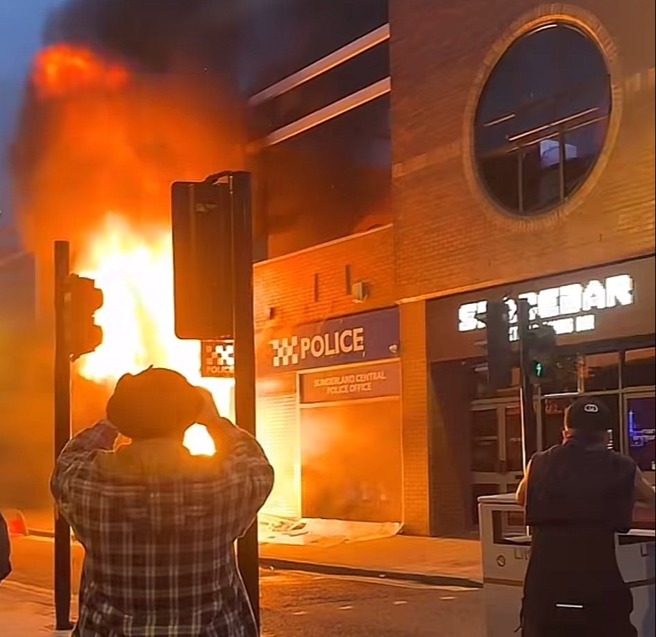 a phone screen shows a fire in front of a police building