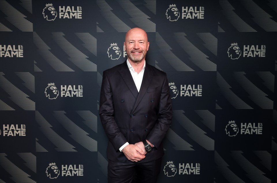 a man in a suit stands in front of a wall that says hall of fame