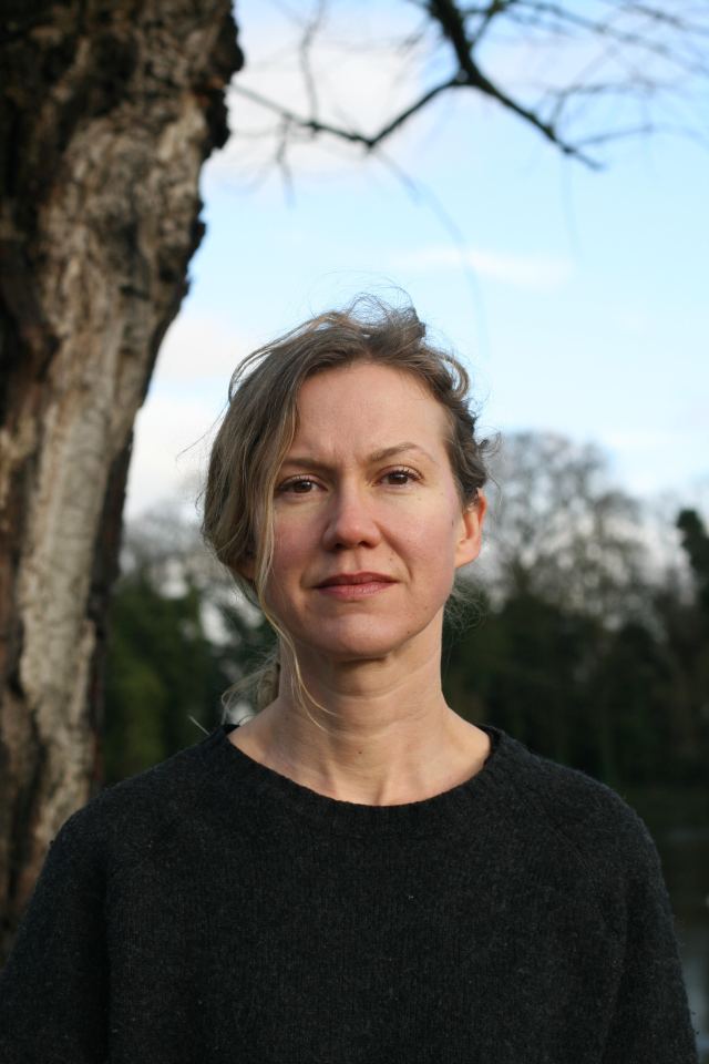 a woman in a black sweater stands in front of a tree