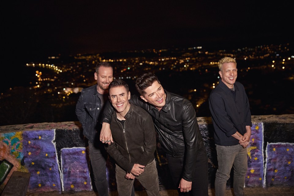 four men are posing for a picture in front of a graffiti wall