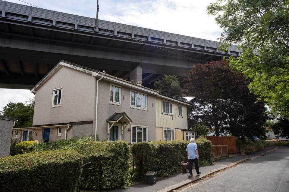 a man walking a dog in front of a house under a bridge