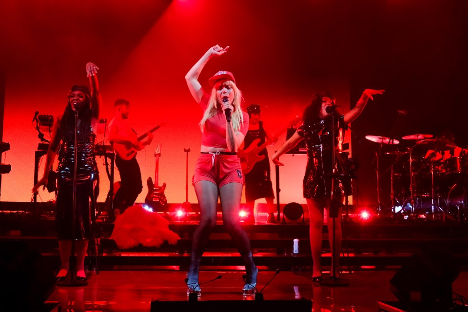 a woman singing into a microphone wearing a red hat with the letter r on it