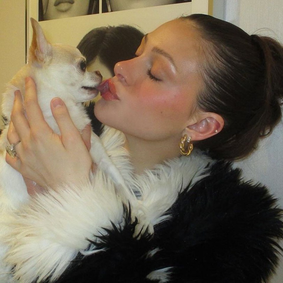 a woman kisses a small white dog on the cheek
