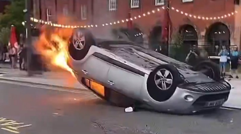 a car is on its side with flames coming out of it .