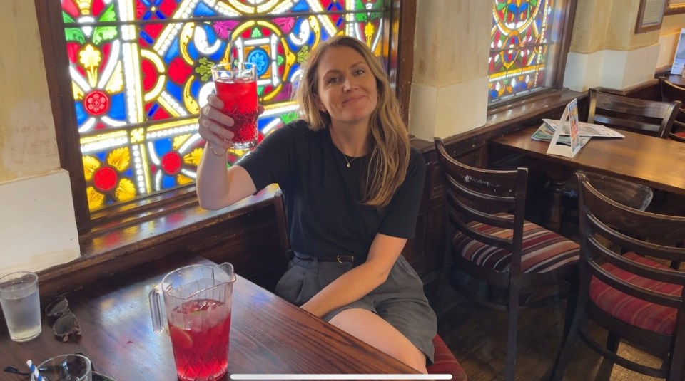 a woman sitting at a table with a pitcher of red liquid in front of a stained glass window