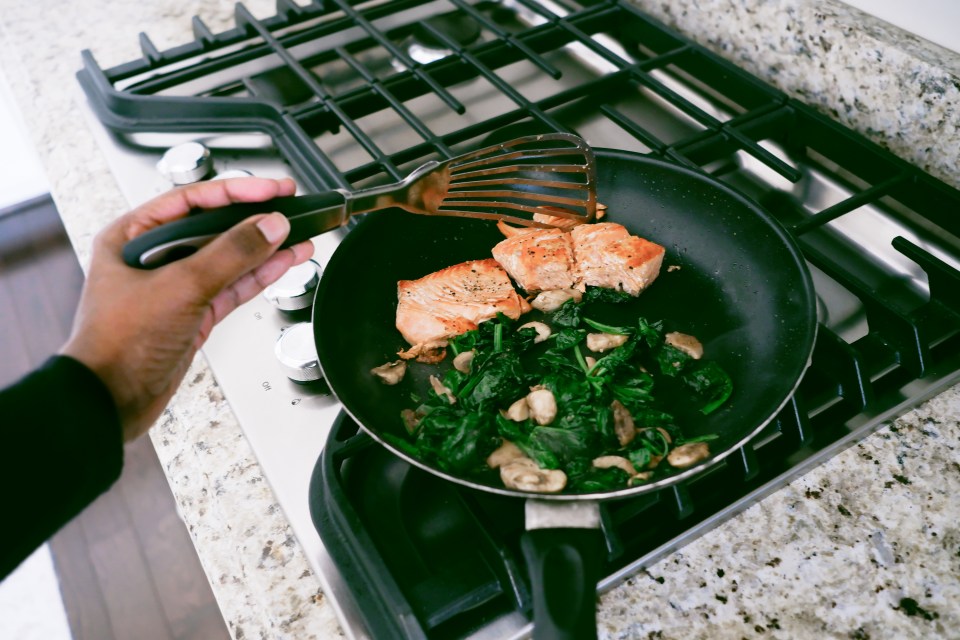 a person is cooking salmon and spinach in a frying pan