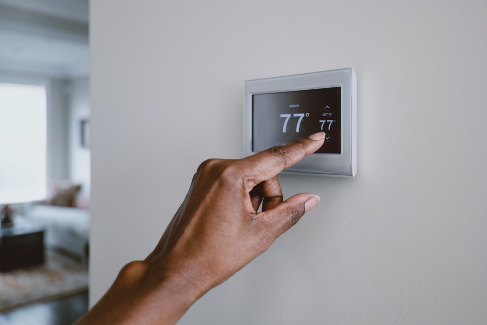 a person is adjusting a thermostat to 77 degrees