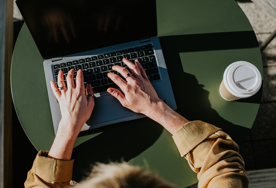 a person typing on a laptop with a cup of coffee on the table
