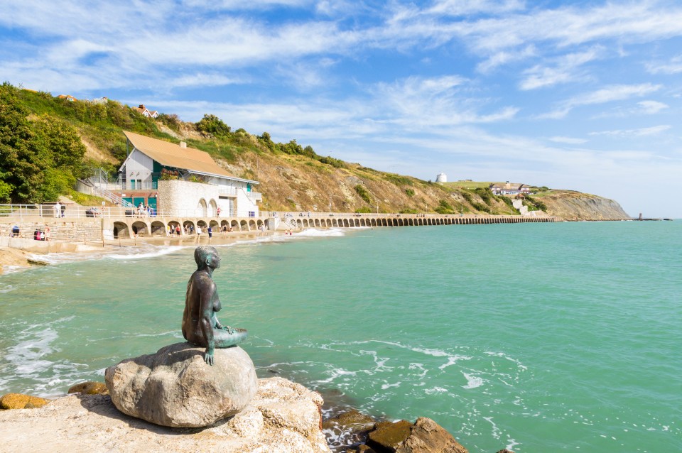 a statue of a mermaid sits on a rock near the ocean