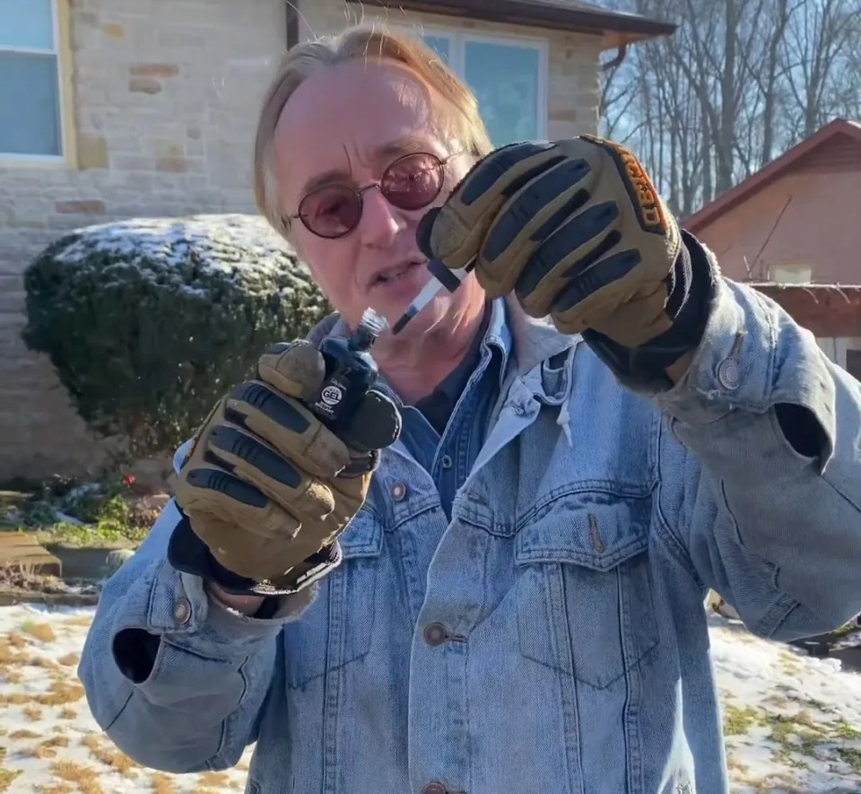 a man in a denim jacket and gloves holds a screwdriver