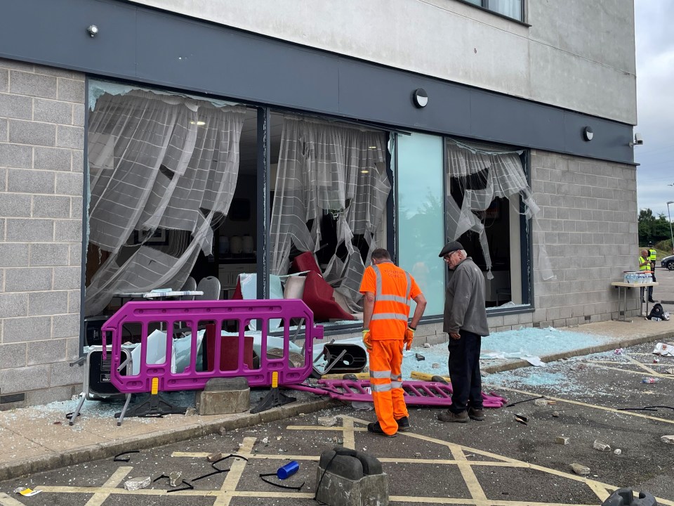 a man in an orange vest stands in front of a broken window