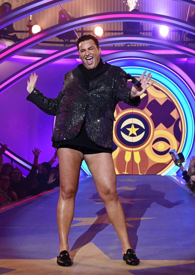 a man in shorts and a sequined jacket stands on a stage