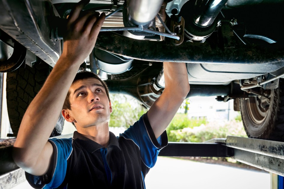 a man in a blue shirt is working on the underside of a car