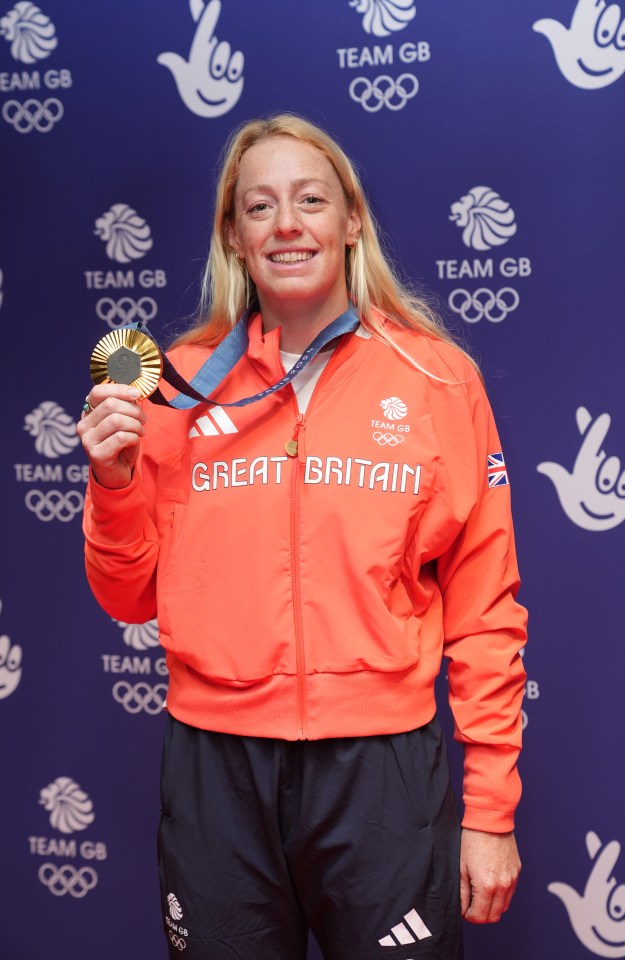 a woman wearing a great britain jacket holds a gold medal