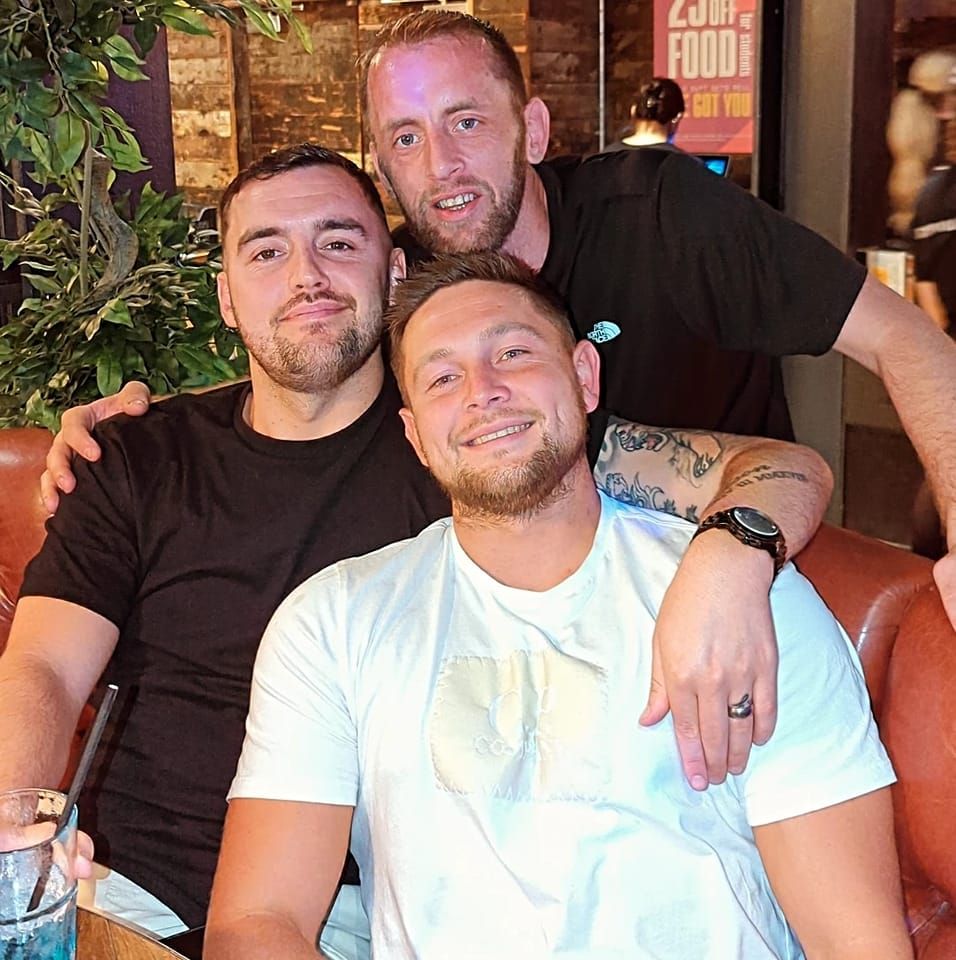 three men are posing for a picture in front of a sign that says food
