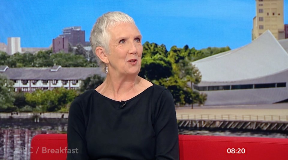 a woman sits on a red couch in front of a screen that says bbc breakfast