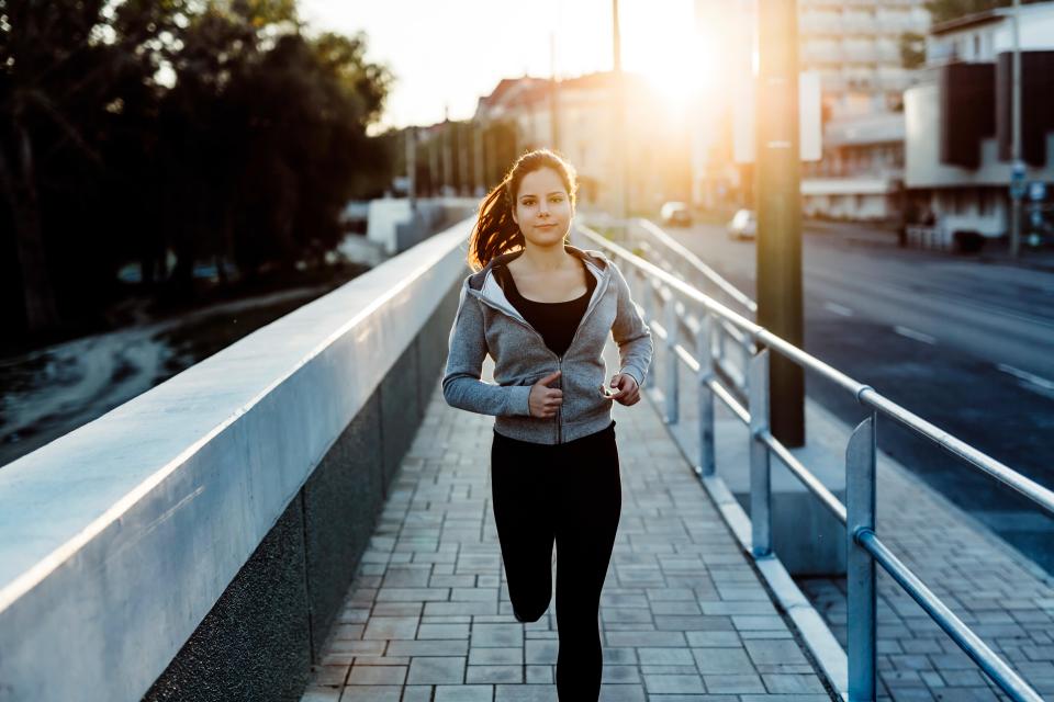 a woman in a grey jacket is running on a bridge
