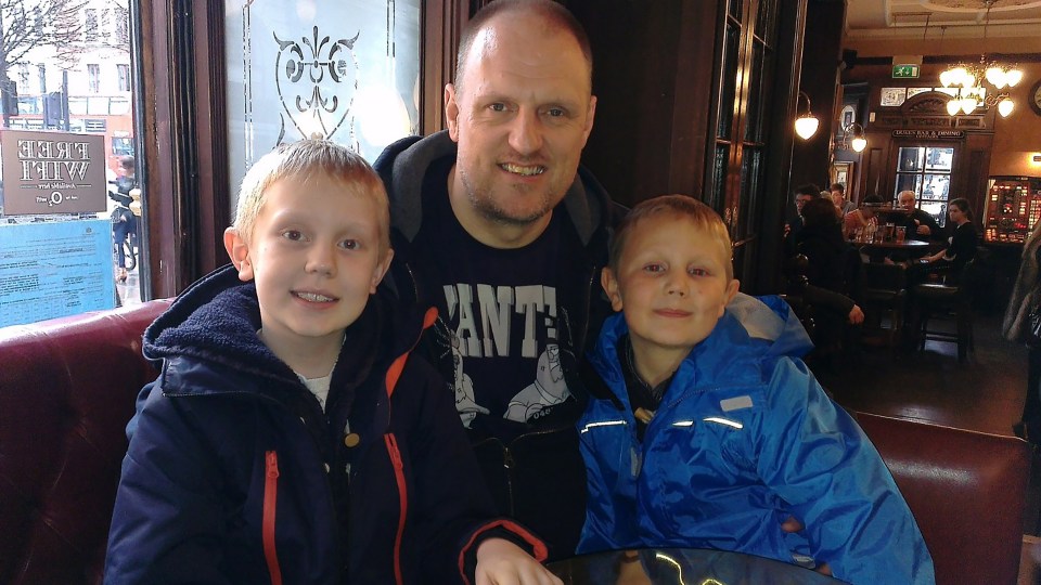 a man wearing a shirt that says " ante " poses with two young boys