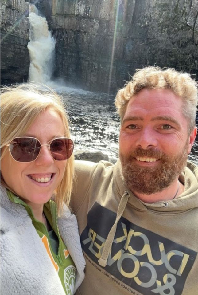 a man and a woman are posing for a picture in front of a waterfall