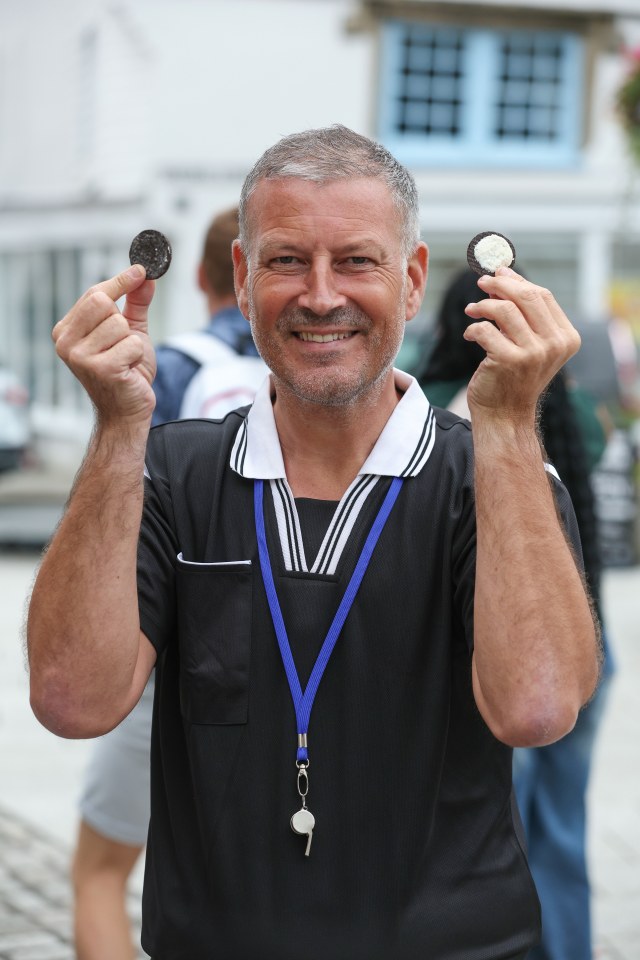 a man wearing a black shirt and a blue lanyard holds two oreos in his hands