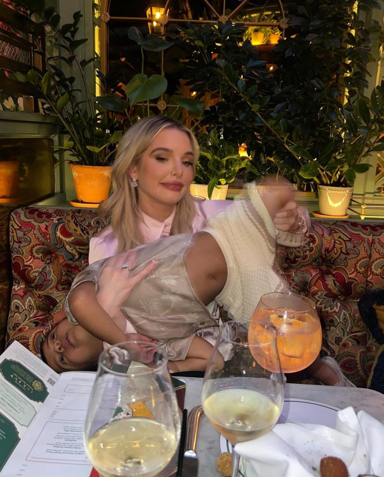 a woman holds a child while sitting at a table with glasses of wine