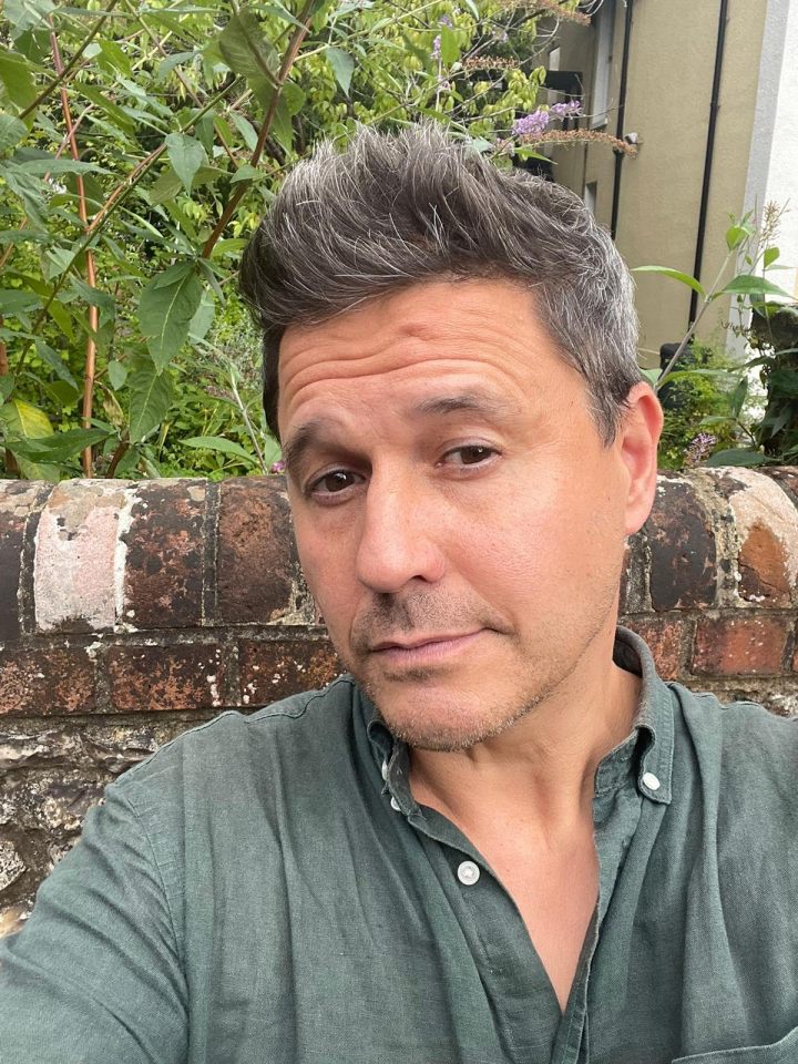 a man in a green shirt stands in front of a brick wall