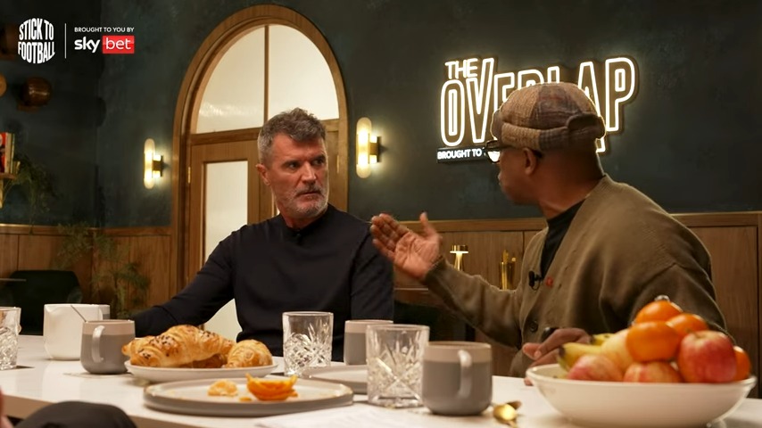 two men sit at a table in front of a sign that says the overlap