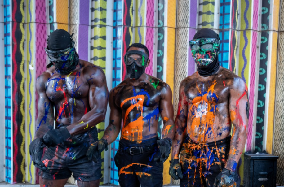three men with their bodies covered in paint are standing in front of a colorful wall